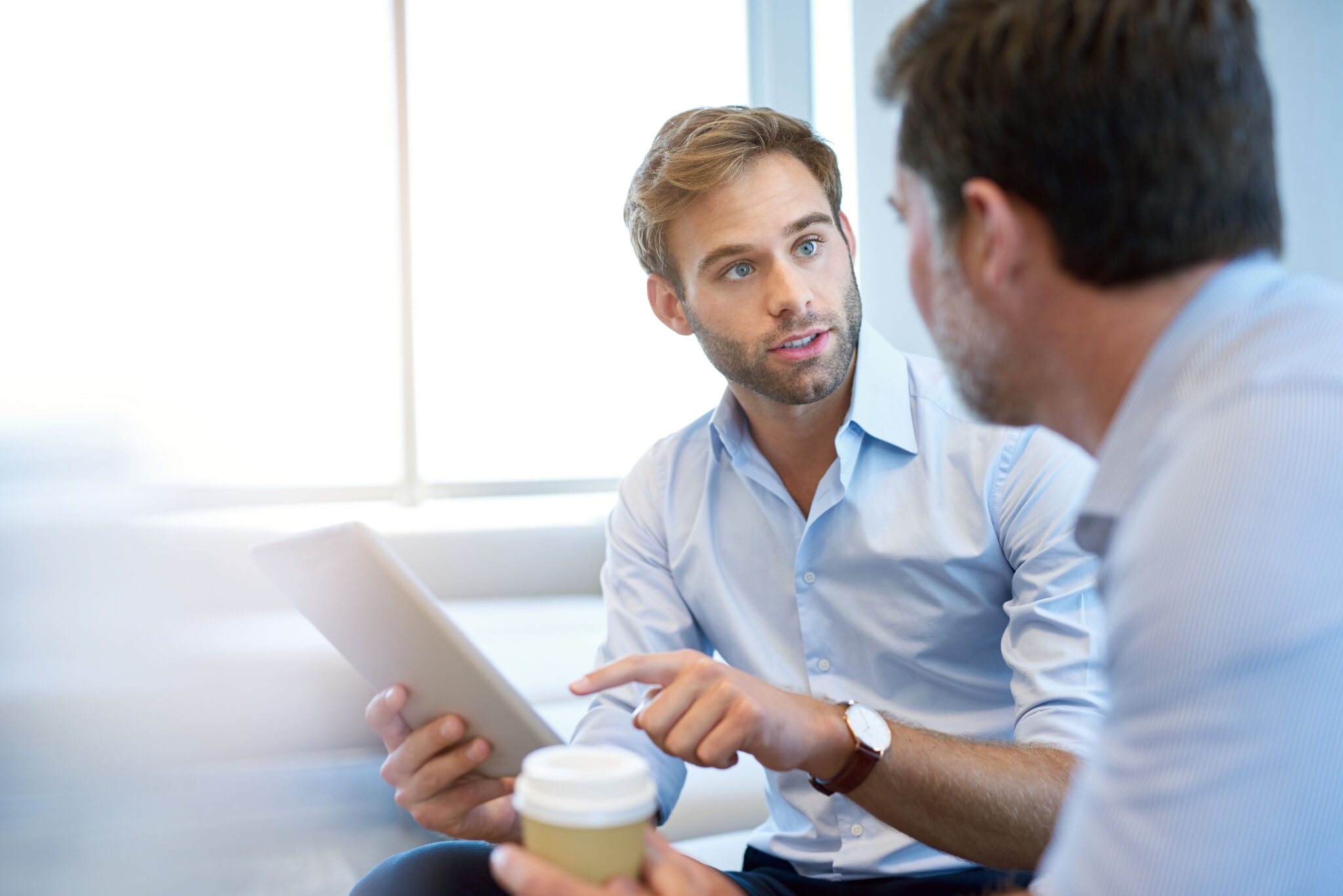 Handsome young business entrepreneur holding a digital tablet while talking about ideas with his mature corporate manager