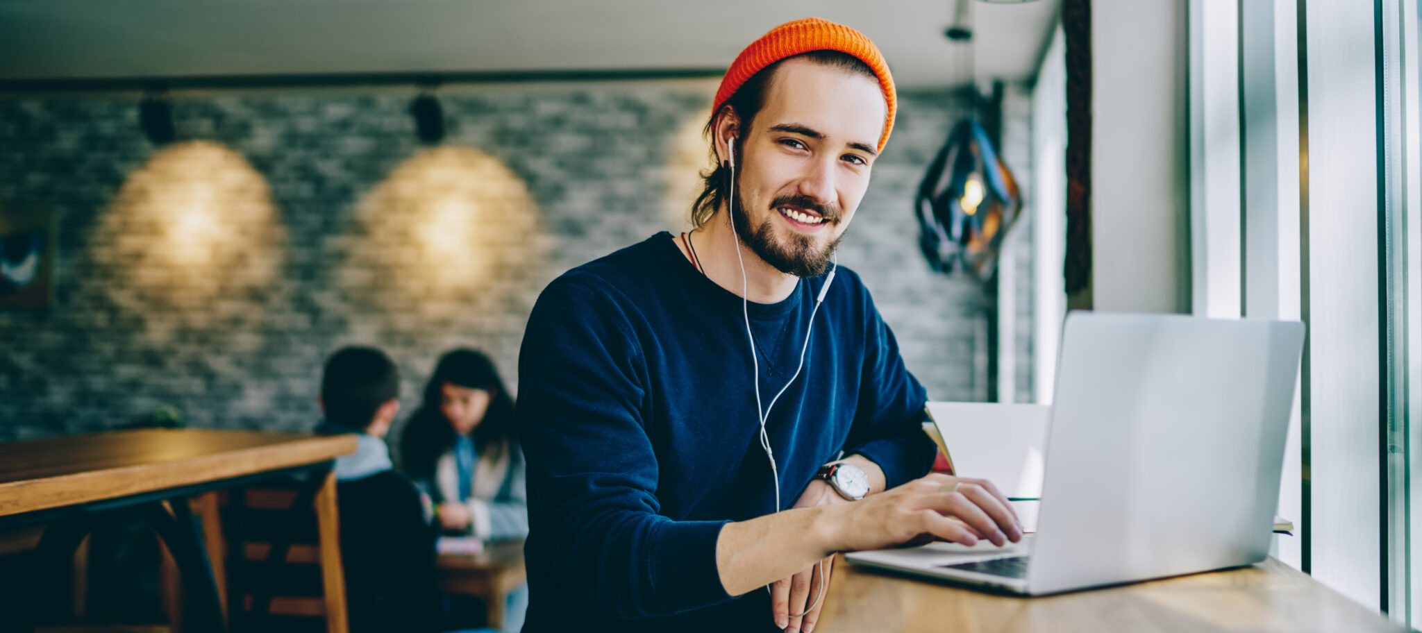 Portrait of happy smiling hipster guy enjoying time for favourite music playlist during e learning in cafeteria, positive male teenager in headphones rest indoors sitting at table with laptop device