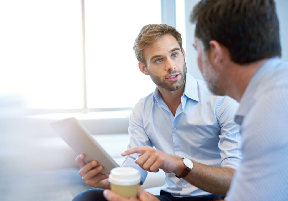 Handsome young business entrepreneur holding a digital tablet while talking about ideas with his mature corporate manager